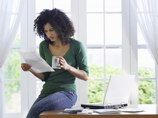 Displeased African American woman reading document with a coffee cup on desk