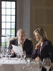 Businessman and woman sitting at restaurant table and reading documents