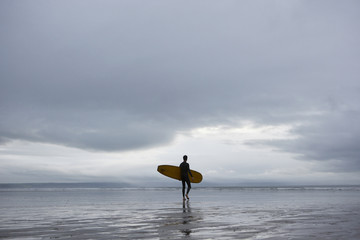 Full length of young male surfer with surfboard walking towards sea on beach