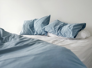 Fototapeta na wymiar Morning view of an unmade bed with crumpled blue bed linens and no people