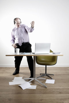 Full Length Of Businessman Wearing Headphones While Playing Air Guitar At Office Desk