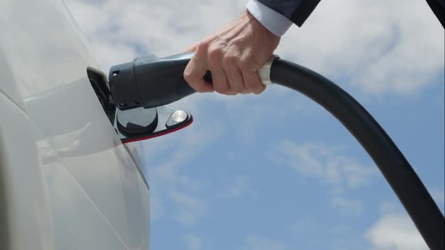CLOSE UP: Businessman plugging in white electric car at charging station