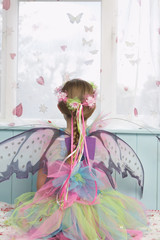 Rear view of a young girl in fairy costume looking through window