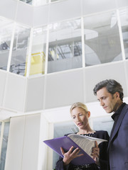 Low angle view of two business people looking at folder in office atrium