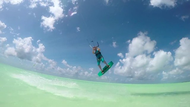 SLOW MOTION: Extreme kite surfer jumping high over camera showing shaka sign