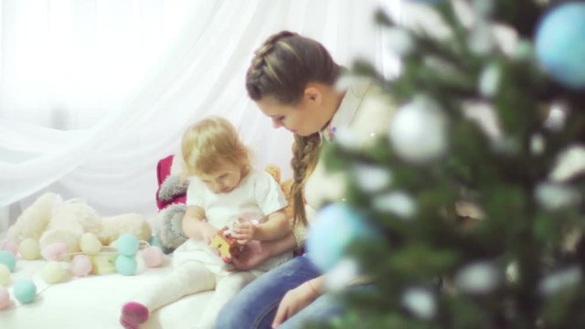 Happy young mother playing with her sweet baby in a decorated room near the christmas tree