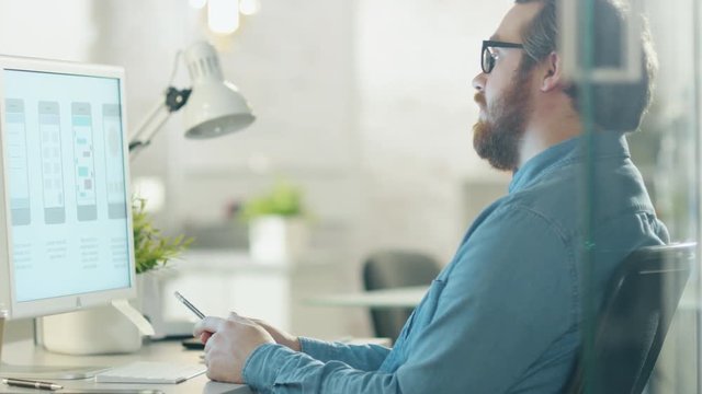 Focused Creative Man Thinks while Sitting at His Workplace Desk. He Holds Pencil and Looks at Desktop Computer Screen.  Shot on RED Cinema Camera in 4K (UHD).