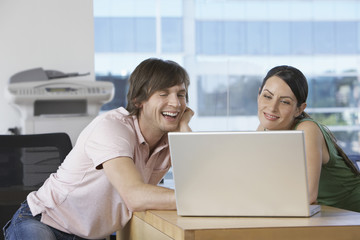 Cheerful business colleagues using laptop at desk in office