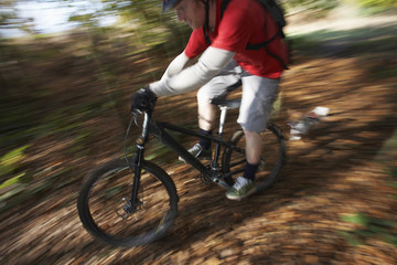 Naklejka premium Blurred motion of dog chasing man on mountain bike through forest