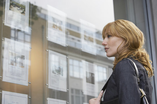 Side View Of A Young Woman Looking At Window Display At Real Estate Office