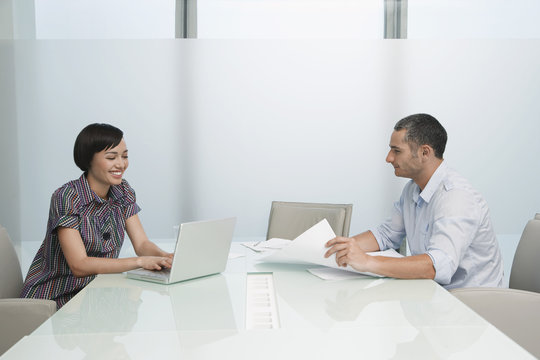Side view of a man and smiling woman working in conference room with documents and laptop