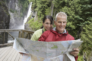 Mature man and woman reading map with waterfall in the background