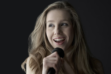 Closeup of happy teenage girl singing into microphone on black background