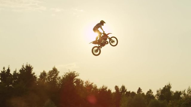 SLOW MOTION: Extreme pro motocross biker jumps dusty big air kicker over the sun