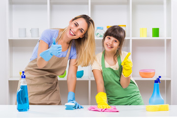 Happy mother and her daughter showing thumb up while cleaning together.