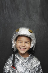 Portrait of a cute young boy in aluminum foil astronaut costume smiling against black background