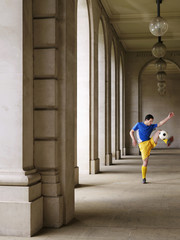 Full length of a soccer player kicking ball in portico