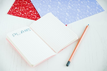 Flat lay of blank notepad for make plans, pencil, decorated Christmas papers. on a white table. Perspective view. New year resolution planning 