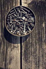 Filtered screws and bolts in tin can on wooden background