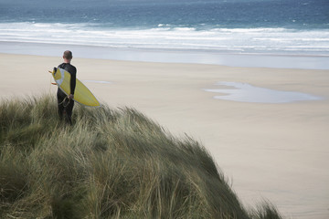 Rear view of male surfer with surfboard on beach looking at sea