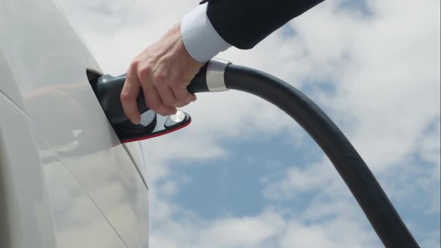 Close up businessman plugging out white electric car at charging station