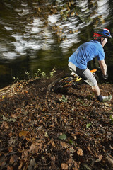 Low section of young man riding mountain bike through forest