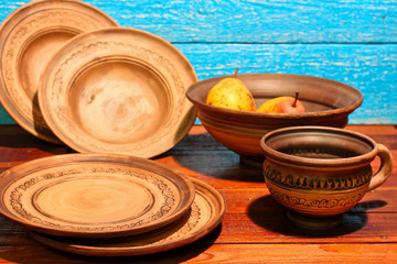 Empty brown clay plates, bowls, mug with ornament pattern on a blue wooden background. Ukraine