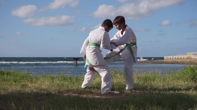 Young people, children, athletes, sport activity, combat and extreme sports, latino boys exercising in karate and traditional martial arts. Simulation of fight on the beach near the sea