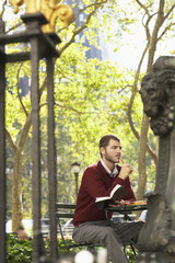 Thoughtful young businessman holding book and pen in park