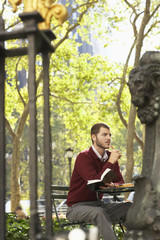 Thoughtful young businessman holding book and pen in park