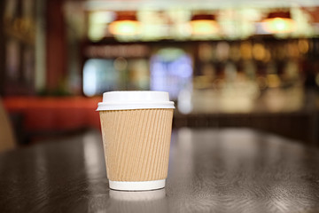 Paper cup with tasty coffee on wooden table in cafe, close up view
