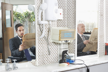 Two businessmen reading newspapers while waiting for haircut in hair salon