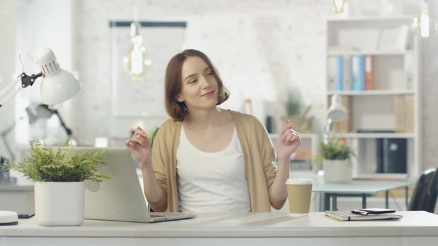 Creative Young Woman Dances while Sitting at Her Workplace Desk. She Sits in a Light and Modern Office Place. Shot on RED Cinema Camera in 4K (UHD).