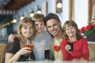 Portrait of happy young parents and children with drinks at restaurant