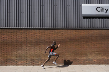 Side view of a man running past brick wall with 'city' written on it