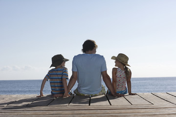 Rear view of a man with two children sitting on jetty