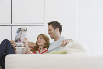 Side view of a cheerful and relaxed young couple reading brochure on sofa