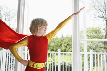 Young boy in superhero costume with arm extended indoors