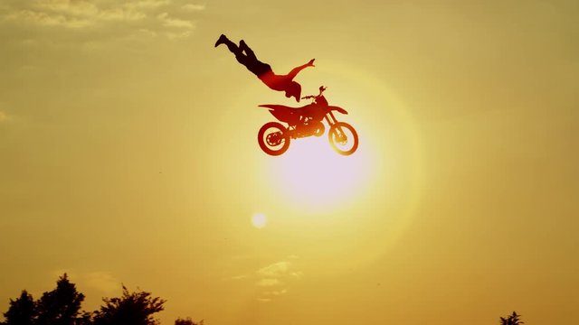 SLOW MOTION: Pro motocross biker jumping no hands superman against sunset sky