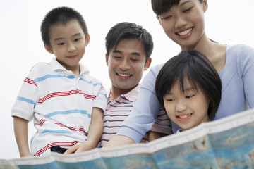 Low angle view of happy parents with children looking at map against sky
