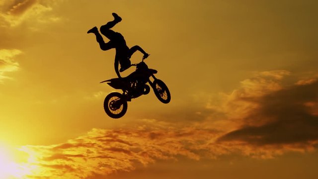 SLOW MOTION CLOSEUP: Extreme motocross biker jumping freestyle trick at sunset