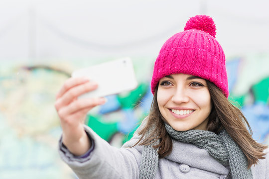 Beautiful teenage girl in pink beanie taking a selfie on smart phone in winter