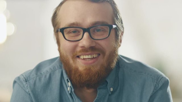 Happy Young Ginger Bearded Man Wearing Glasses Smiles Into the Camera. Bright Lights In the Background.  Shot on RED Cinema Camera in 4K (UHD).