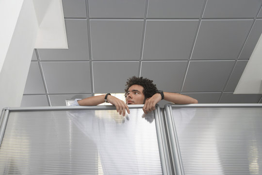 Young male office worker peering over cubicle wall in the office