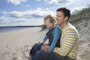 Fototapeta na wymiar Happy father and daughter sitting on sandy beach