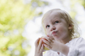 Closeup portrait of a little blond girl eating apple outdoors