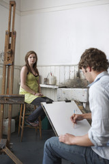 Male student sketching female model in art class