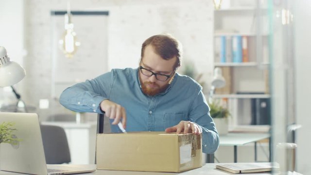 Creative Man Opens Up Parcel While Sitting in His Bright and Modern Office.  Shot on RED Cinema Camera in 4K (UHD).