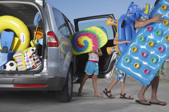 Father And Two Children Unloading Beach Accessories From Car