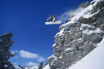 Low angle view of a person on snowboard jumping midair over cliff